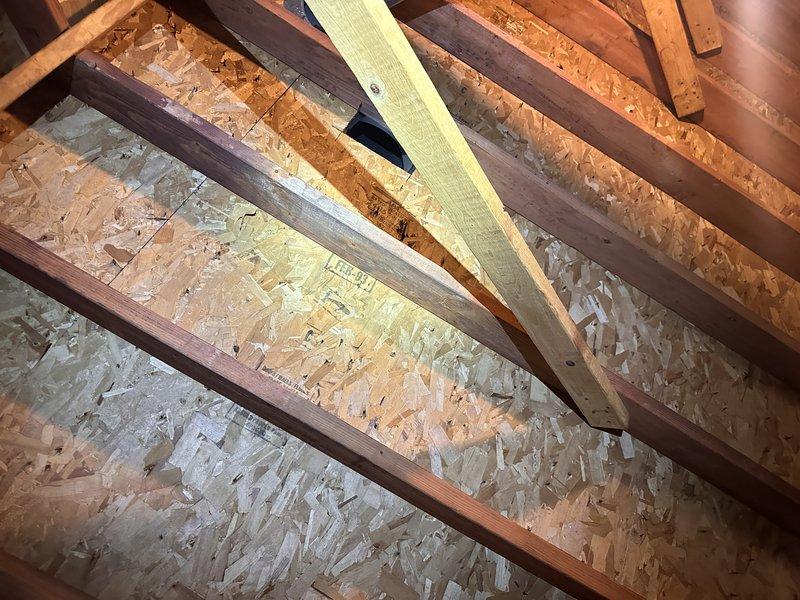 Conducted attic assessment for ventilation and insulation improvements. Evaluated existing attic space with exposed rafters, wooden planking, and HVAC ductwork with reflective insulation, noting minimal pink fiberglass insulation coverage on attic floor and exposed joists. Inspected roof structure including trusses, beams, and OSB sheathing to determine feasibility for gable vent installation and prepared estimate for proper attic ventilation system and blown insulation installation to improve indoor air quality and energy efficiency.