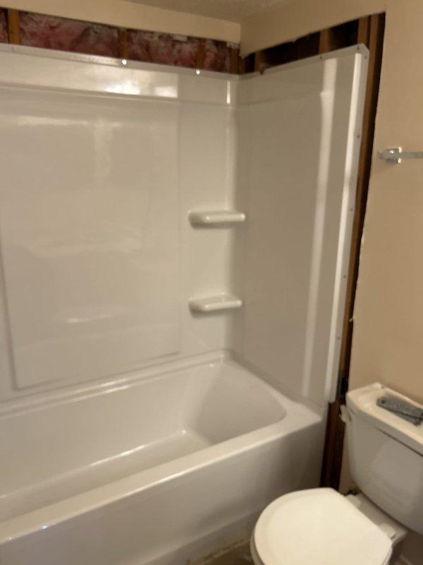 Completed full shower/tub installation on second floor of vacant property, installing a 30x60 white left-hand fiberglass tub-shower combination unit. Removed existing tile and knockdown walls down to studs, then installed new knockdown wall system as base for tub surround. Installed new Delta shower valve body with chrome trim kit, Delta chrome tub spout, and Watco waste and overflow assembly. Ran all necessary copper water supply lines to shower valve and tub spout, connecting to existing building supply. Installed drain piping including P-trap and waste connections to tie into existing drain system. All plumbing connections tested and verified leak-free under pressure. Work area cleaned and all debris removed upon completion.