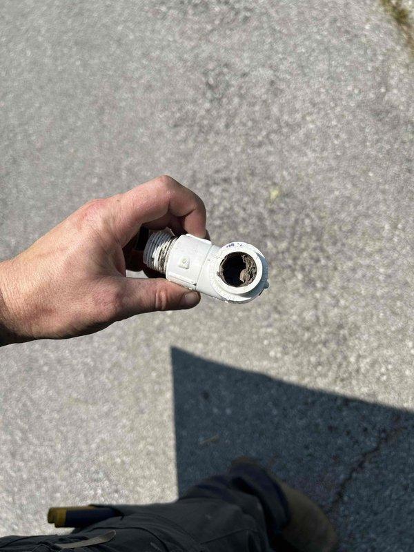 # HVAC Service Report - Water Leak Repair

Responded to service call for active water leak from air conditioning system. Upon arrival, confirmed water leaking onto floor from 13-year-old AC unit that was otherwise cooling properly.

Conducted thorough inspection of the condensate drainage system and identified failed drain fitting as the source of the leak. The compromised fitting was allowing condensate water to bypass the drain line and discharge directly onto the floor. Removed the defective black threaded metal and white plastic compression fitting component.

Installed new drain fitting to restore proper condensate drainage. Verified all connections were secure and leak-free. Tested system operation to confirm water was draining correctly through the condensate line without any further leakage. Inspected surrounding area for any water damage, noting moisture staining on insulation material at floor level in the unit location.

System restored to normal operation with proper conden