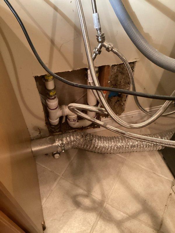 Responded to water leak originating from washing machine supply lines affecting kitchen area. Upon arrival, accessed plumbing cavity through wall to identify source of leak. Investigation revealed compromised flexible supply line connections at washer hookup location. Removed wall access panel to expose mechanical chase containing water supply lines, drain system, and associated plumbing components. 

Inspection identified active leak from deteriorated braided stainless steel supply hose connections. Water intrusion had caused visible staining and discoloration on PVC drain piping within wall cavity. Shut off water supply at isolation valves to prevent further water damage. Removed failed supply lines and assessed condition of connection points and shutoff valves. 

Installed new braided stainless steel washing machine supply hoses with proper torque specifications at both fixture and valve connections. Tested all connections under full pressure to verify leak elimination. Inspected su