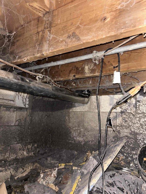 Installed complete dryer vent system from interior basement location to exterior wall termination. Routed 4-inch metal ductwork through crawl space using five sections of rigid pipe and four 90-degree elbows to navigate around floor joists and existing utilities. Secured all connections with foil tape to ensure airtight seal and proper airflow. Terminated vent through red brick exterior wall with black louvered vent cap for weather protection and proper exhaust discharge.