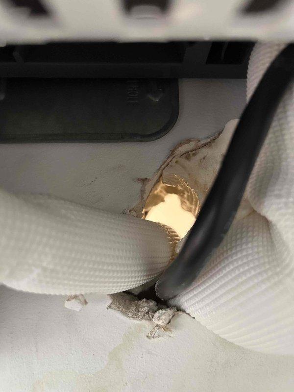 Responded to mini split callback for water leaking down wall. Previous technicians identified condensate drain line backfeeding due to improperly positioned drain hole drilled too high. Inspected drainage system and documented existing conditions showing corrugated drain hose configuration and damaged insulation on refrigerant lines with moisture staining. Verified drain line routing and evaluated previous correction attempts to determine additional remediation needed for proper condensate removal.