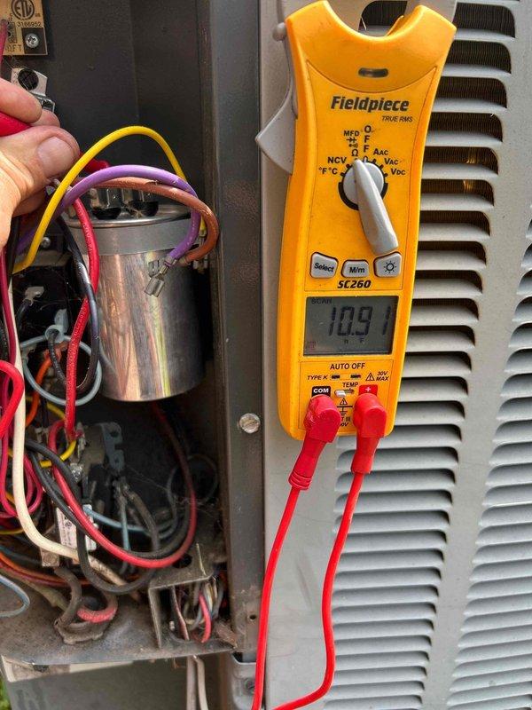 Responded to no cooling complaint on 10-year-old electric HVAC system with air circulation but no cooling capability. Performed electrical diagnostics on outdoor condensing unit using clamp meter and multimeter. Testing revealed failed run capacitor with readings outside acceptable parameters. Measured existing TITAN PRO 370 VAC capacitor (model TRC-FD45S) showing improper capacitance values of 10.9 and 44.5 microfarads, indicating capacitor failure preventing compressor from operating properly. Verified all electrical connections at capacitor terminals and confirmed compressor circuit integrity. Replaced defective dual run capacitor with new unit matching original specifications. Restored power to system and verified proper compressor startup and operation. Confirmed adequate cooling air temperature at supply registers and normal system amperage draw. System operating within manufacturer specifications upon departure.
