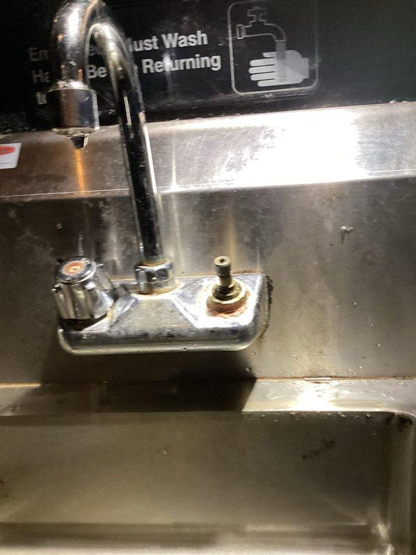 Responded to commercial plumbing service call for mysterious basement leak investigation and bathroom fixture repair. Inspected commercial kitchen area with stainless steel sink and pre-rinse spray faucet assembly, noting visible rust staining and discoloration around mounting hardware that indicated potential leak source. Assessed multi-compartment commercial sink with gooseneck faucet showing typical wear patterns and water staining, evaluated fixture condition and functionality to determine repair versus replacement recommendations.