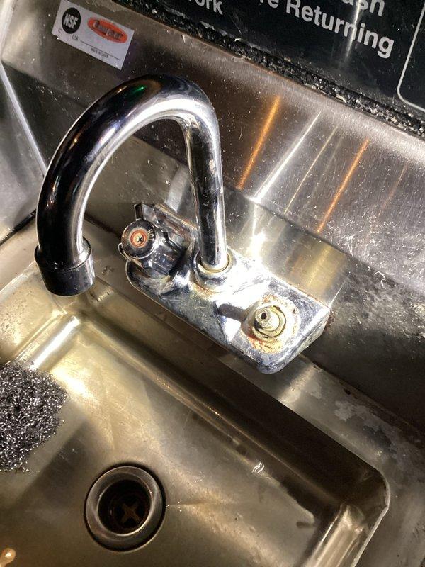 Responded to commercial plumbing service call for mysterious basement leak investigation and bathroom fixture repair. Inspected commercial kitchen area with stainless steel sink and pre-rinse spray faucet assembly, noting visible rust staining and discoloration around mounting hardware that indicated potential leak source. Assessed multi-compartment commercial sink with gooseneck faucet showing typical wear patterns and water staining, evaluated fixture condition and functionality to determine repair versus replacement recommendations.