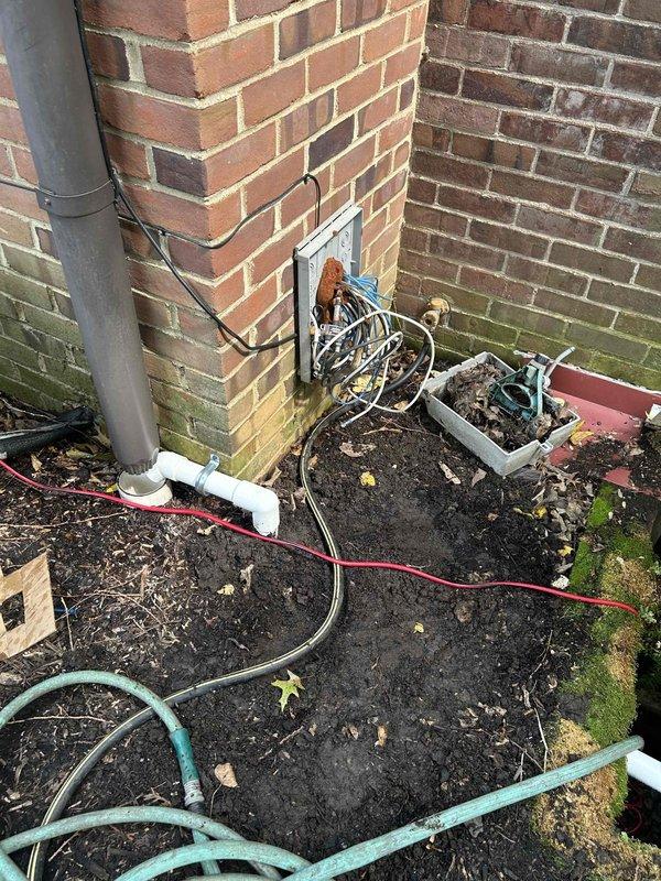 Installed new outdoor sump pump system to address flooding issues at basement window well. Excavated 6-8 inches below grade and set pump basin with sump pump unit. Ran PVC discharge line vertically through wooden window well structure and terminated into existing gutter system with proper air gap to prevent backflow. System tested and operational upon completion.