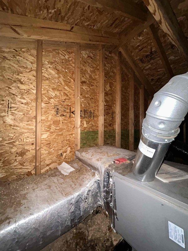 Responded to water leak complaint with water streaming down wall from attic causing drywall separation at seam. Upon inspection of attic-mounted HVAC system, photographed equipment and surrounding area to document conditions. Attic space showed exposed framing with spray foam insulation, metallic ductwork with reflective insulation, and air handler unit with connected flexible ducting. OSB wall sheathing exhibited greenish discoloration indicating moisture staining or potential mold growth. Documented all findings with photographic evidence for further evaluation and repair recommendations.