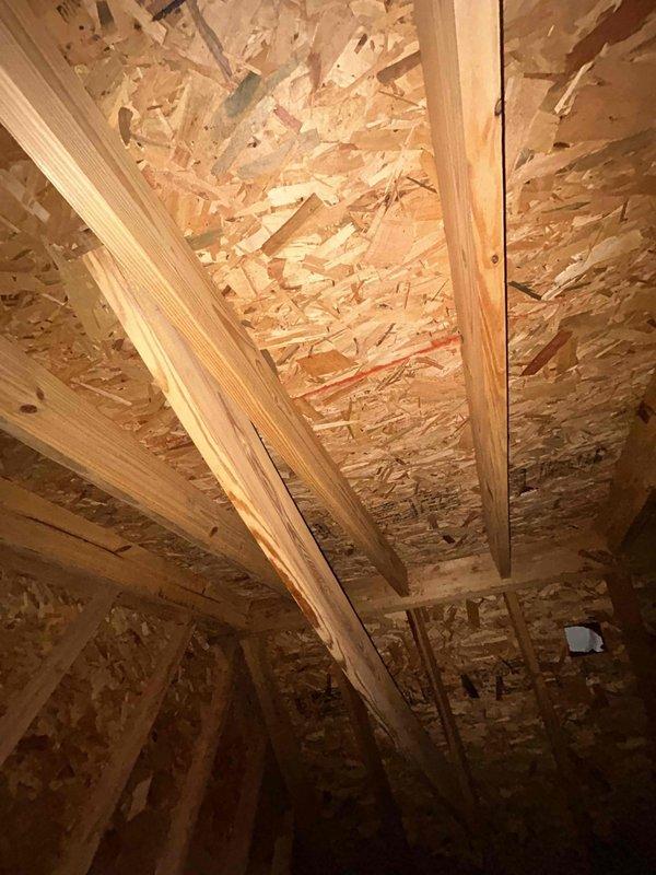 Responded to water leak complaint with water streaming down wall from attic causing drywall separation at seam. Upon inspection of attic-mounted HVAC system, photographed equipment and surrounding area to document conditions. Attic space showed exposed framing with spray foam insulation, metallic ductwork with reflective insulation, and air handler unit with connected flexible ducting. OSB wall sheathing exhibited greenish discoloration indicating moisture staining or potential mold growth. Documented all findings with photographic evidence for further evaluation and repair recommendations.