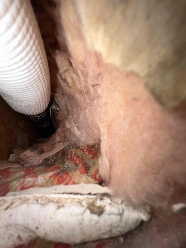 Responded to water leak complaint at indoor HVAC unit in sunroom that had been leaking for several days. Unit was off upon arrival. Performed diagnostic inspection and discovered condensate drain line issue with visible mineral deposits and buildup at drain connection point. Inspected attic space and ductwork, finding pink fiberglass insulation with signs of water damage and discoloration around affected area. Documented conditions with photographs showing deteriorated drain fitting with crusty residue accumulation and water-damaged insulation materials. Identified source of water intrusion coming from behind unit due to compromised condensate drainage system.