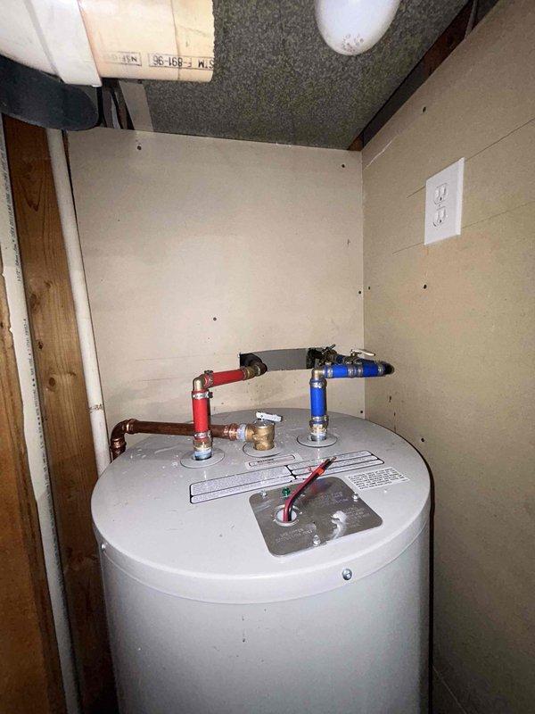 Completed full replacement of residential tanked water heater in utility closet installation. Removed existing unit and installed new white cylindrical water heater with proper clearances and code-compliant connections. Connected hot and cold water supply lines using copper piping with red-handled and blue-handled shut-off valves at unit top for isolation capability. Verified gas supply connection with yellow ball valve shut-off mechanism and black iron gas pipe with properly sealed threaded connections. Ensured all plumbing connections were secure and leak-free, with water heater properly positioned within confined closet space. Installation includes standard electrical connection via wall outlet and meets manufacturer specifications for residential water heating system operation.