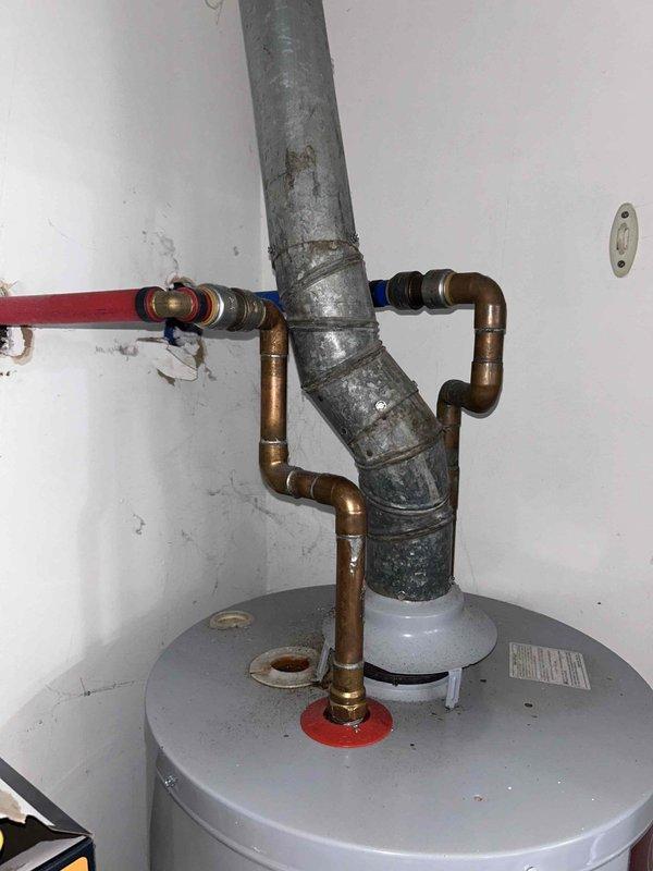 Responded to service call for 4-5 year old tanked water heater experiencing pilot light failure and inability to heat water. Upon arrival, inspected unit located in kitchen closet utility area. Assessed gas supply line connections, thermocouple assembly, and pilot assembly for proper function. Noted corroded galvanized piping and aged copper connections in the installation. Tested thermocouple output voltage and inspected gas control valve for proper operation. Cleaned pilot orifice and burner assembly to remove debris and carbon buildup. Verified proper venting through black exhaust flue pipe. Adjusted thermocouple positioning for optimal flame contact. Cycled pilot light multiple times to confirm stable ignition and flame retention. Tested main burner operation and verified water heating functionality restored. Inspected all gas line connections with leak detection solution to ensure system safety.