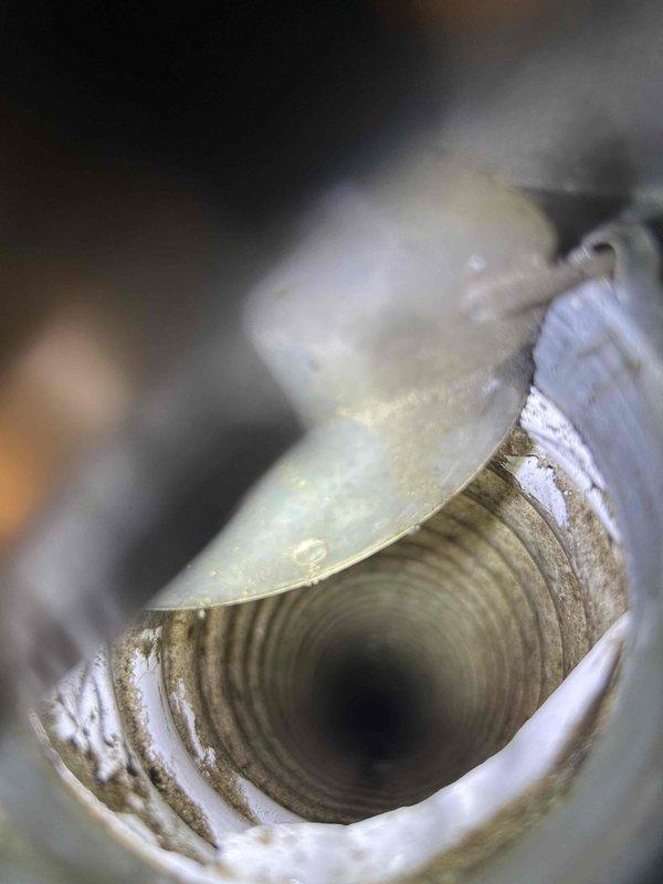 Responded to water leak complaint at second-floor bathroom ceiling vent in 3-story residential property with 10-year-old HVAC system and furnace located in attic space above affected area. Inspected bathroom exhaust vent housing and flexible ductwork, confirming moisture intrusion originated from HVAC condensate drainage issue rather than plumbing system. Documented conditions with photos showing vent assembly and interior duct surfaces with visible water staining and debris accumulation.