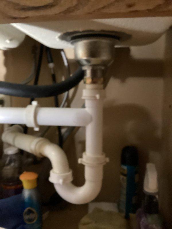 Responded to kitchen sink drain leak that began several days prior. Upon arrival, provided 30-minute advance notice as requested. Accessed cabinet beneath kitchen sink and inspected white PVC P-trap assembly and connections. Identified leak source at drain pipe junction under sink basin. Verified leak was isolated to kitchen plumbing only with no issues affecting other household fixtures.

Examined metallic sink drain basket connection to P-trap assembly and checked all compression fittings and slip joints for proper seal. Inspected black rubber dishwasher or disposal connection hose for potential contribution to leak. Tightened loose slip nut connections on P-trap where leakage was occurring. Verified all PVC fittings were properly seated and compression washers were intact.

Cleared under-sink cabinet area of cleaning supplies and household items to ensure proper access to plumbing components. Tested drain system by running water through sink and monitoring all connections for contin