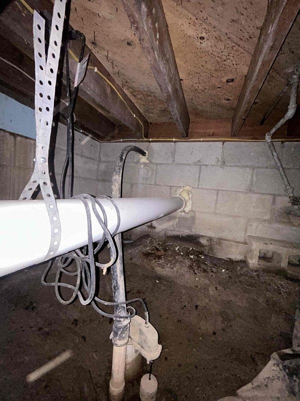 Completed plumbing inspection of basement crawl space to assess water line relocation needs and evaluate condition of existing piping system. Inspected water supply lines currently routed through wooden structural members requiring repositioning to meet code compliance and prevent future damage. Documented aging galvanized and steel pipes showing significant deterioration, corrosion, and discoloration throughout the system. Evaluated existing PVC drainage lines and mounting hardware for structural integrity. Assessed accessibility constraints within crawl space including exposed floor joists, concrete block foundation walls, and limited clearance areas. Photographed current pipe routing, support bracket locations, and areas requiring replacement to provide comprehensive documentation for estimate preparation and future repair work.