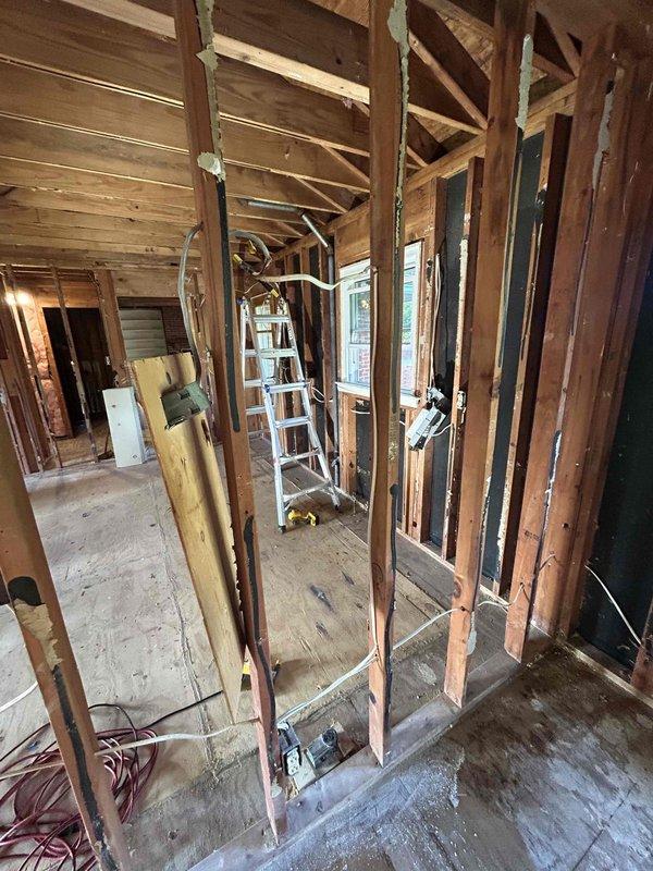 Completed comprehensive electrical estimate for full rewire of residential property currently under renovation. Assessed exposed framing in multiple areas including attic/crawl space and main living spaces where structure has been stripped to studs. Evaluated existing wiring conditions, documented cable routing through floor joists and wall cavities, and identified electrical device locations including mounted equipment between ceiling joists. Photographed current state of electrical infrastructure including visible white and dark-colored conductors running through open wall cavities. Provided detailed assessment for complete electrical system replacement including new circuit routing, device placement, and code-compliant installation throughout the gut-renovated space.