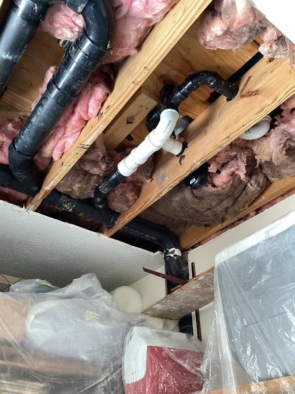 Responded to ceiling water leak complaint and performed inspection of overhead plumbing system. Accessed attic space and examined exposed piping infrastructure, including black PVC drain lines and white PVC connections running through ceiling joists. Inspected pipe joints, fittings, and connections for signs of active leakage or moisture damage. Documented existing plumbing configuration with fiberglass insulation present between joists. Protected customer belongings with plastic sheeting during investigation and completed photographic documentation of plumbing system for service records.