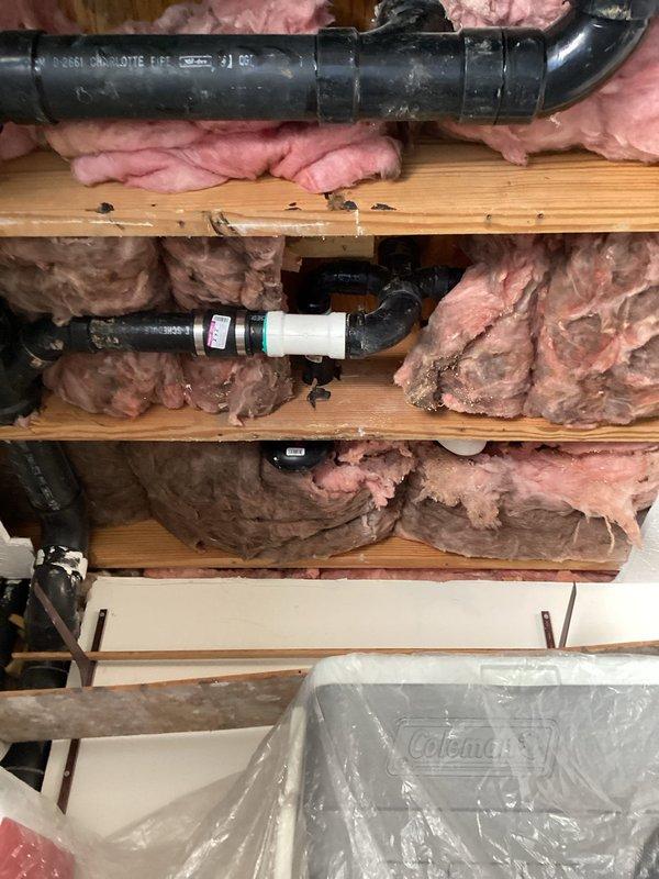 Responded to ceiling water leak complaint and performed inspection of overhead plumbing system. Accessed attic space and examined exposed piping infrastructure, including black PVC drain lines and white PVC connections running through ceiling joists. Inspected pipe joints, fittings, and connections for signs of active leakage or moisture damage. Documented existing plumbing configuration with fiberglass insulation present between joists. Protected customer belongings with plastic sheeting during investigation and completed photographic documentation of plumbing system for service records.