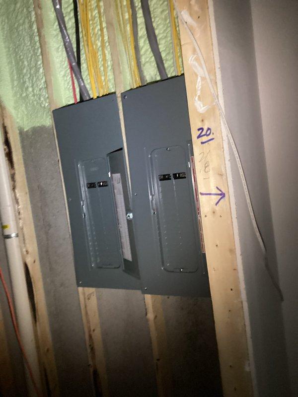 Conducted comprehensive electrical estimate for generator installation at residential property currently under construction. Assessed existing electrical infrastructure including dual panel boxes mounted on exposed wall framing with spray foam insulation, evaluating capacity and compatibility for generator integration. Documented exterior site conditions including drainage pathway with corrugated pipes and available space between structures for potential generator placement. Photographed electrical panels showing multiple wire runs and circuit configurations to determine connection requirements and transfer switch specifications needed for backup power system installation.