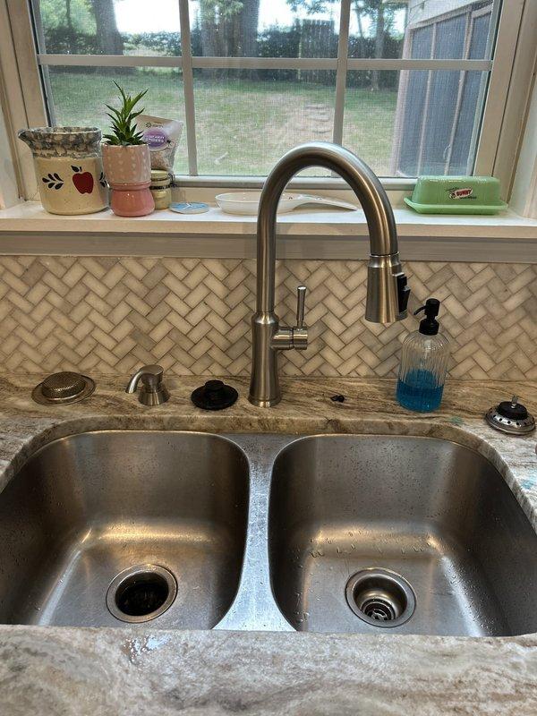 Completed comprehensive kitchen sink plumbing upgrade including replacement of existing drain trap and discharge assembly with new PVC piping in proper P-trap configuration while maintaining existing garbage disposal unit. Removed old water supply lines and installed new copper supply piping with soldered connections and new shutoff valves for both hot and cold water lines. Successfully installed customer-supplied brushed nickel pull-down kitchen faucet with high arched spout on double-basin stainless steel sink. All connections tested and verified leak-free, with proper water flow and drainage confirmed upon completion.