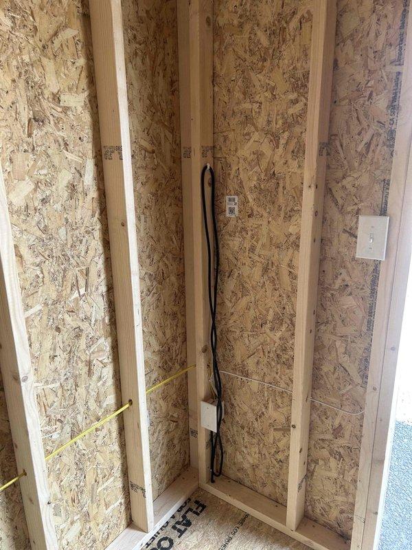 Completed electrical rough-in installation for new construction outbuilding, installing GFCI receptacle, standard duplex outlet, single-pole switch, keyless light fixture with bulb, and SJ cord with male cord cap. Routed black electrical cable vertically through wall cavities between studs, mounted outlet boxes to framing members per code requirements, and verified all connections prior to insulation and drywall installation.