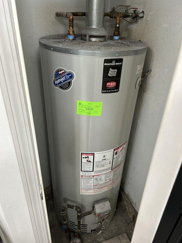 Completed plumbing estimate for commercial water heater replacement in utility closet. Assessed existing 75-gallon gas-fired Bradford White tank water heater with standard venting and copper supply lines. Documented current installation including top-mounted flue vent, dual shut-off valves with blue handles, gas control valve assembly, and proper grounding connections for replacement specifications.