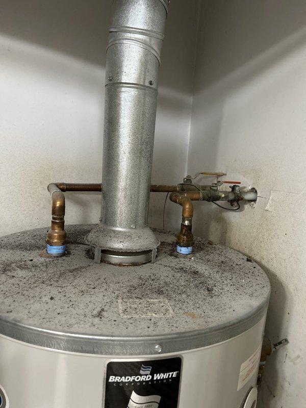 Completed plumbing estimate for commercial water heater replacement in utility closet. Assessed existing 75-gallon gas-fired Bradford White tank water heater with standard venting and copper supply lines. Documented current installation including top-mounted flue vent, dual shut-off valves with blue handles, gas control valve assembly, and proper grounding connections for replacement specifications.