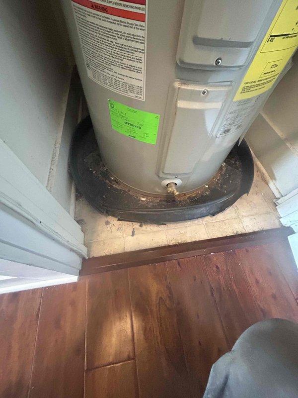 Performed comprehensive assessment of existing 38-gallon short electric storage tank water heater located in utility closet. Documented current unit specifications and installation conditions through photographic evidence. Inspection revealed significant rust and corrosion on drip pan beneath water heater, with extensive water damage and staining present on surrounding flooring materials including both tile and adjacent hardwood surfaces. Observed moisture-related discoloration extending from base of unit, indicating active or recent leaking condition. Evaluated utility closet installation space, clearances, and existing plumbing connections to provide accurate replacement estimate for customer consideration of tank or tankless water heater options.