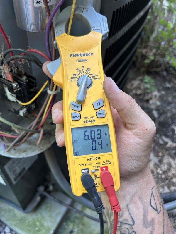 Responded to no cool complaint on three-year-old upstairs system with attic-mounted air handler. Performed diagnostic testing on outdoor condensing unit using clamp meter to measure compressor amperage and voltage readings. Measurements indicated compressor operating at 6.03 amps with 0.4 volts initially, then recorded secondary reading of 7104 on refrigerant line. Documented electrical connections and component operation with photos for service records.