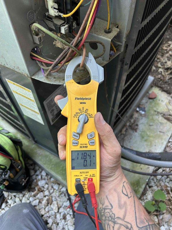 Responded to no cool complaint on three-year-old upstairs system with attic-mounted air handler. Performed diagnostic testing on outdoor condensing unit using clamp meter to measure compressor amperage and voltage readings. Measurements indicated compressor operating at 6.03 amps with 0.4 volts initially, then recorded secondary reading of 7104 on refrigerant line. Documented electrical connections and component operation with photos for service records.