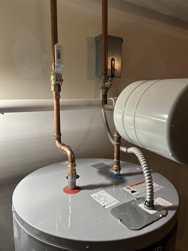 Conducted comprehensive assessment of residential tanked water heater following improper installation by previous contractor. Inspection revealed severe corrosion at base connections and pipe penetration points, with extensive mineral buildup and oxidation damage to copper piping and floor surfaces. Documented corroded plumbing connections at water heater top, including compromised brass fittings and deteriorated pipe joints where improper installation techniques had accelerated corrosion. Photographed evidence of water damage, rust staining, and structural deterioration at floor level. Evaluated condition of electrical connections, safety valves, and overall system integrity to determine viability of repair versus full unit replacement. Provided detailed estimate options for corrective action to address failed connections and restore system to code-compliant operation.