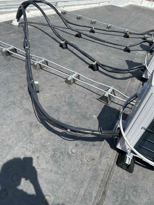 Returned to site to replace temporary post blockers under refrigerant linesets with permanent Durablock supports on commercial rooftop HVAC installation. Successfully installed proper elevation blocks beneath curved lineset runs to ensure adequate clearance from roof membrane and maintain professional appearance of mechanical system routing.