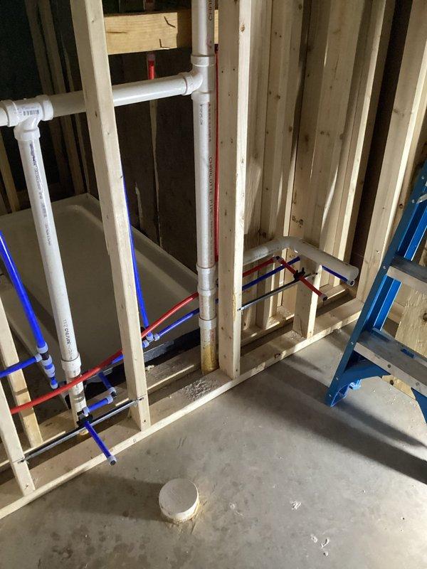 Completed comprehensive plumbing rough-in installation for two bathroom renovation project. Installed new sewage ejector pump and verified proper functionality before departure.

**Bathroom A (Shower):**
Jackhammered concrete flooring to access drainage area. Installed new P-trap assembly with stub-up for shower base connection. Ran and stubbed out Uponor water supply lines for lavatory, toilet, and shower connections. Installed Delta universal rough-in shower valve with Uponor fittings per specifications.

**Bathroom B (Tub & Shower):**
Ran complete Uponor water supply lines for lavatory, toilet, and tub/shower valve connections. Installed Delta universal rough-in tub/shower valve with Uponor fittings. Set new shower base and installed tub/shower wall panels. Ran stub-out for lavatory drain connection.

All water supply lines installed using new Uponor PEX piping system with hot and cold lines properly color-coded and secured to framing. All rough-in valves and drain connections teste