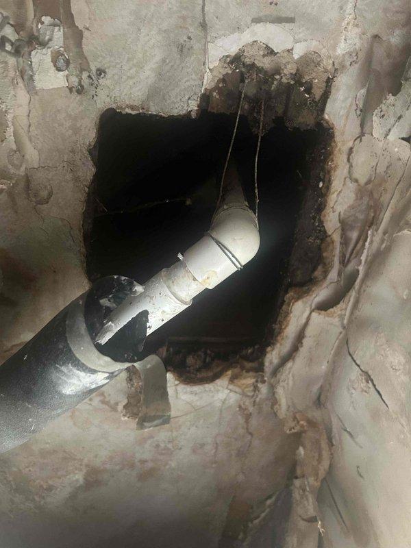 Responded to water leak from indoor HVAC unit located in second-floor drop ceiling that had been actively leaking since 2am. Upon arrival, found significant water damage to ceiling structure with compromised drywall, visible water staining, and structural deterioration around the affected area. Accessed the unit through damaged ceiling section where PVC condensate drain line and flexible ductwork were exposed. Inspection revealed extensive moisture damage to wooden framing members and support beams in the ceiling cavity, with severe discoloration and deterioration indicating prolonged water exposure. Documented all damage with photographic evidence showing compromised wall surfaces, exposed plumbing infrastructure, and affected structural components. Identified source of water intrusion and assessed extent of damage to both HVAC components and building structure for repair recommendations.