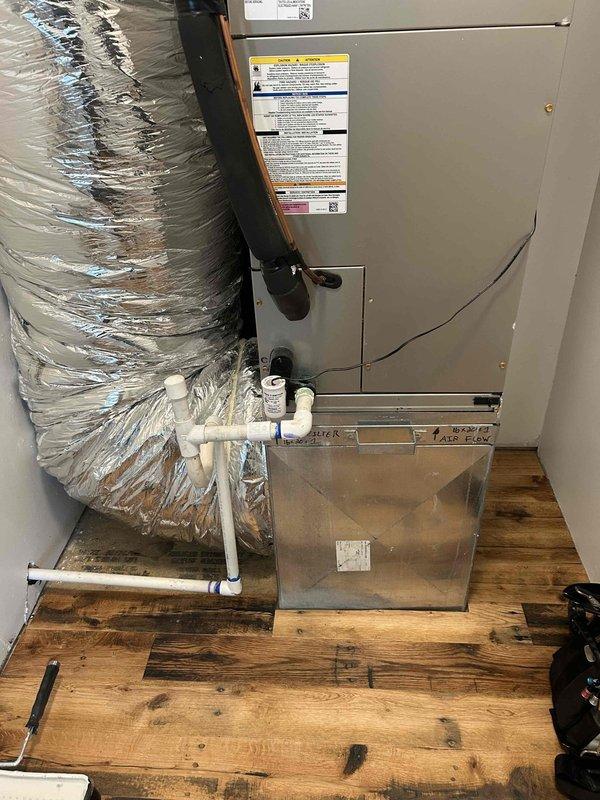 Responded to water leak at indoor air handler unit located in closet. Upon inspection, found condensate drain line had separated at connection point, causing water damage to surrounding flooring and ductwork. Disassembled and removed damaged drain line components. Cleaned and prepared connection points, then reinstalled new PVC drain line with proper fittings and secure connections. Verified proper drainage flow and tested system operation. Inspected air handler unit and surrounding copper refrigerant lines for any additional moisture damage or corrosion. Confirmed unit operational and condensate draining properly into drain pan and through newly installed drain line without leaks.