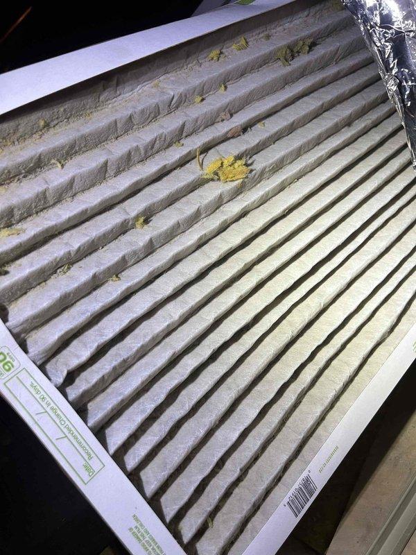 Responded to no cooling complaint on electric HVAC system with indoor unit located in attic. Upon arrival, thermostat was set to 70°F with indoor temperature reading 76°F. Performed system diagnostic and inspected air filter, which showed moderate accumulation of dust and debris with visible yellow particulate matter throughout pleated media. Replaced dirty air filter with new filter to restore proper airflow. Adjusted thermostat cooling setpoint to 65°F to bring system online. Verified system startup sequence initiated properly with 2-minute delay timer engaged for compressor protection. System operational at time of departure.