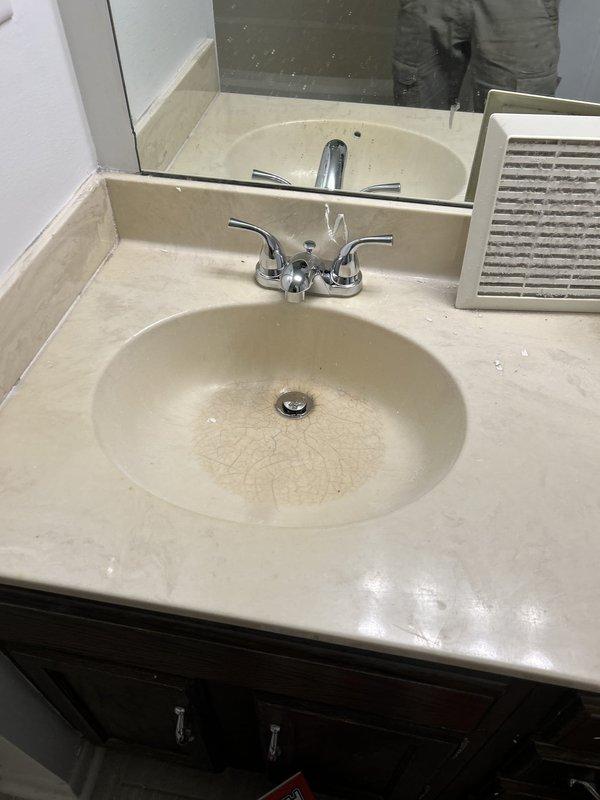 Replaced two customer-supplied chrome centerset lavatory faucets in vacant property bathroom. Both faucets were two-handle models with lever-style handles and curved spouts, installed on beige cultured marble vanity tops with integrated oval basins. Completed installations per manufacturer specifications and verified proper operation and leak-free connections.