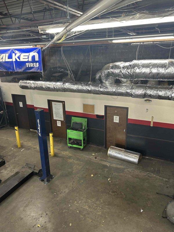 Wrapped spiral ductwork system in tire shop facility with R8 foilback insulation on both supply and return lines to eliminate condensation and leaking caused by high humidity environment contacting cold ductwork during system operation. All seams were sealed with foil tape to prevent temperature loss and ensure proper vapor barrier. Additionally, installed auxiliary drain pan drain line using 3/4" pipe with four 3/4" 90-degree elbows, one 1-1/2" 90-degree elbow, one 1-1/2" bushing to 3/4", and 1-1/2" pipe section to properly route condensate drainage.