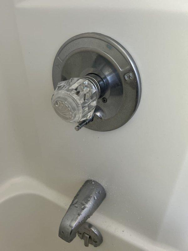 Responded to guest bathroom shower valve issue where water was leaking from the handle assembly when shower was activated. Upon inspection, identified compromised valve stem seal and escutcheon assembly allowing water to bypass through the handle mechanism rather than directing flow properly through the spout and diverter. Disassembled single-handle shower control valve, examined internal components including cartridge, stem seals, and trim assembly. Documented existing fixture condition showing brushed metal escutcheon with clear acrylic handle and gray tub spout with diverter below. Assessed valve cartridge for wear and proper seating within the rough-in body to determine repair feasibility versus full replacement recommendation.