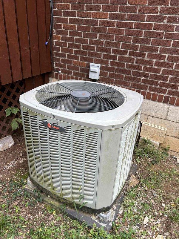 Responded to no cooling call on 5-year-old standard split system with gas furnace and basement air handler. Customer reported outdoor condenser unit not operating and system blowing warm air. Upon arrival, confirmed supply air temperature at register measured 84.9°F, indicating no cooling occurring. Inspected Trane condenser unit exterior, noting unit showed normal weathering for age with algae growth on panels but structurally sound. Diagnosed outdoor unit failure to energize, preventing refrigeration cycle from initiating and resulting in air handler circulating unconditioned air only.