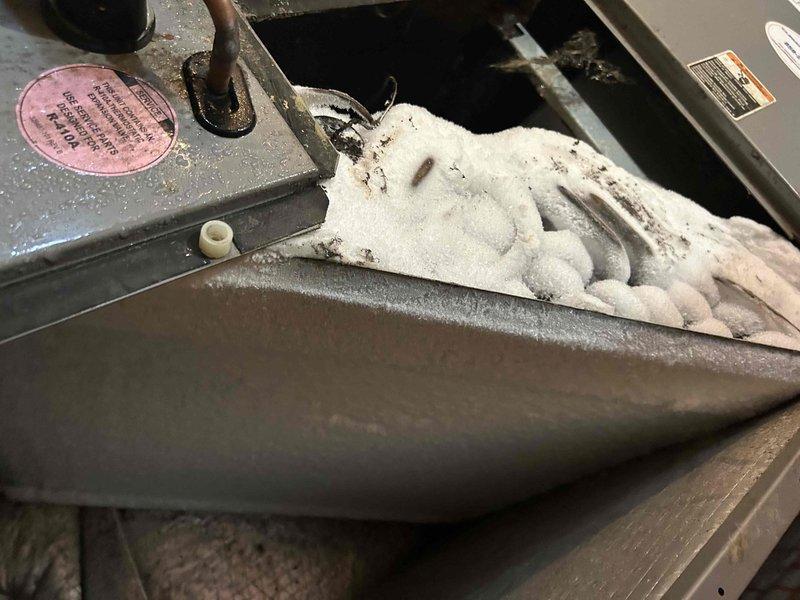 Responded to no cooling complaint on 14-year-old electric air conditioning system. Upon inspection, found evaporator coil completely frozen with extensive ice buildup throughout the indoor unit located in laundry room. Discovered severely restricted airflow caused by heavily contaminated evaporator coil with significant accumulation of dust, debris, and biological growth on coil surfaces. System unable to operate efficiently due to combination of frozen coil condition and obstructed airflow across heat exchanger. Documented conditions with photographs showing extent of ice formation and contamination for customer records.