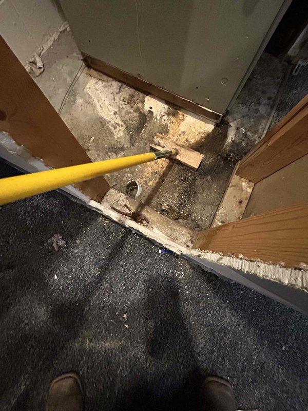 Responded to no cooling call at commercial facility. Found older indoor HVAC unit in basement had overflowed, causing extensive water damage to surrounding carpet and flooring. Upon inspection, discovered significant moisture intrusion had affected subflooring, wall materials, and concrete surfaces in the mechanical room area. Evidence of prolonged water exposure was visible with dark staining and deterioration on wooden framing members, subflooring, and concrete walls. Assessed drainage system failure as source of overflow. Documented extensive damage to building materials including compromised drywall, water-damaged wood framing, and saturated carpeting. Provided floor fan to assist with drying process to mitigate further moisture damage and potential mold growth in affected areas.