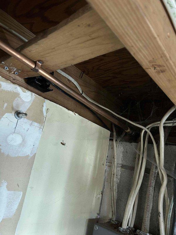 Conducted on-site assessment of existing sump pump discharge system in basement utility area to provide relocation estimate. Evaluated current PVC discharge piping configuration, including horizontal runs along ceiling joists and wall-mounted sections. Inspected mechanical room conditions, noting moisture staining on concrete block walls and existing plumbing infrastructure including copper piping, flexible HVAC ductwork, and electrical systems. Documented exposed ceiling joists, structural framing, and routing pathways for potential discharge line relocation. Photographed current installation to support estimate preparation for municipal discharge system modifications.