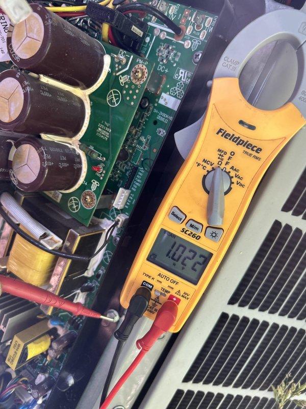 Responded to no cooling call on 7-8 year old electric HVAC system displaying error code 69 (inverter fault) with outdoor fan not operating. Upon arrival, indoor temperature was 80 degrees. Accessed attic-mounted air handler and outdoor condensing unit for diagnostic evaluation.

Performed electrical diagnostics on inverter control board using clamp meter, obtaining voltage readings of 102.3 volts at board terminals. Visual inspection of the green PCB revealed dense population of surface-mounted components including multiple black cylindrical capacitors, integrated circuits, resistors, and copper-coiled inductors. Noted discoloration and brownish residue near center components indicating possible thermal stress or component failure. DC circuit pathways and power supply sections examined for continuity and proper voltage distribution.

Verified outdoor fan motor failure to energize despite power supply to condensing unit. Traced fault to inverter board malfunction preventing proper signa