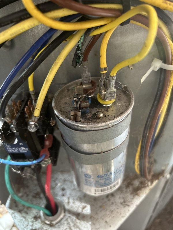 Responded to no cooling call on 5-year-old electric air conditioning system serving master bedroom and basement areas. Upon arrival, thermostat was set to 69°F but indoor temperature measured 74°F, with unit blowing lukewarm air instead of cold air. 

Performed diagnostic inspection of outdoor condensing unit and indoor air handler located in basement. Visual inspection of outdoor unit revealed severely corroded capacitor with significant oxidation and greenish patina on terminal connections. Capacitor showed dark discoloration at connection points with degraded wire terminals. Tested capacitor and confirmed failure, which prevented compressor from starting properly and resulted in loss of cooling capacity.

Replaced failed dual-run capacitor with new OEM-equivalent unit rated for proper microfarad and voltage specifications. Cleaned corroded terminal connections and secured all electrical connections to manufacturer specifications. Cycled system through complete cooling operation and 