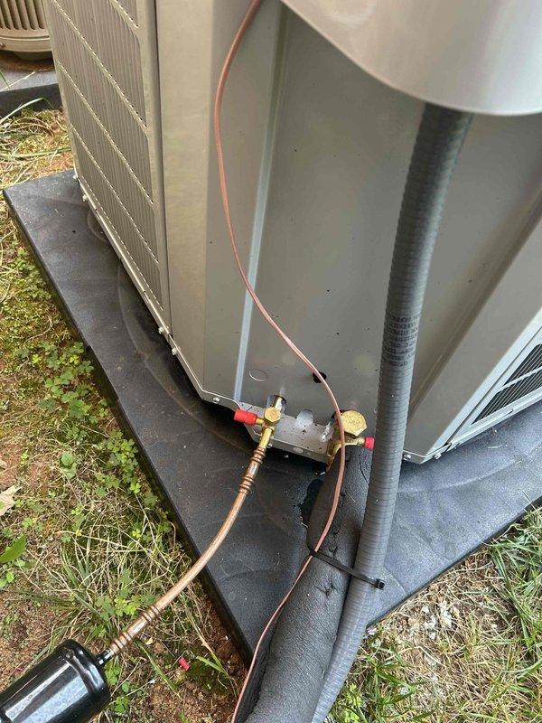 Responded to warranty service call regarding mitigation control placement and thermostat programming concerns. Upon inspection, verified mitigation control device with red connectors is currently positioned on top of outdoor condensing unit with copper refrigerant lines and wiring exposed to elements. Documented current installation configuration with photographs showing unit on concrete pad, flexible conduit routing from wall-mounted disconnect, and overall system layout in side yard location. Addressed concerns regarding upstairs Ecobee thermostat display readings and verified programming parameters for proper system operation.