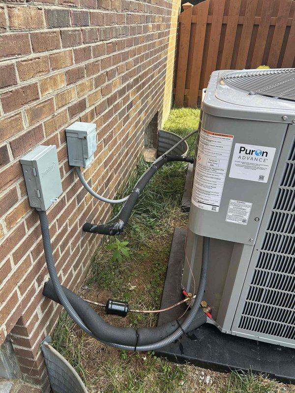 Responded to warranty service call regarding mitigation control placement and thermostat programming concerns. Upon inspection, verified mitigation control device with red connectors is currently positioned on top of outdoor condensing unit with copper refrigerant lines and wiring exposed to elements. Documented current installation configuration with photographs showing unit on concrete pad, flexible conduit routing from wall-mounted disconnect, and overall system layout in side yard location. Addressed concerns regarding upstairs Ecobee thermostat display readings and verified programming parameters for proper system operation.