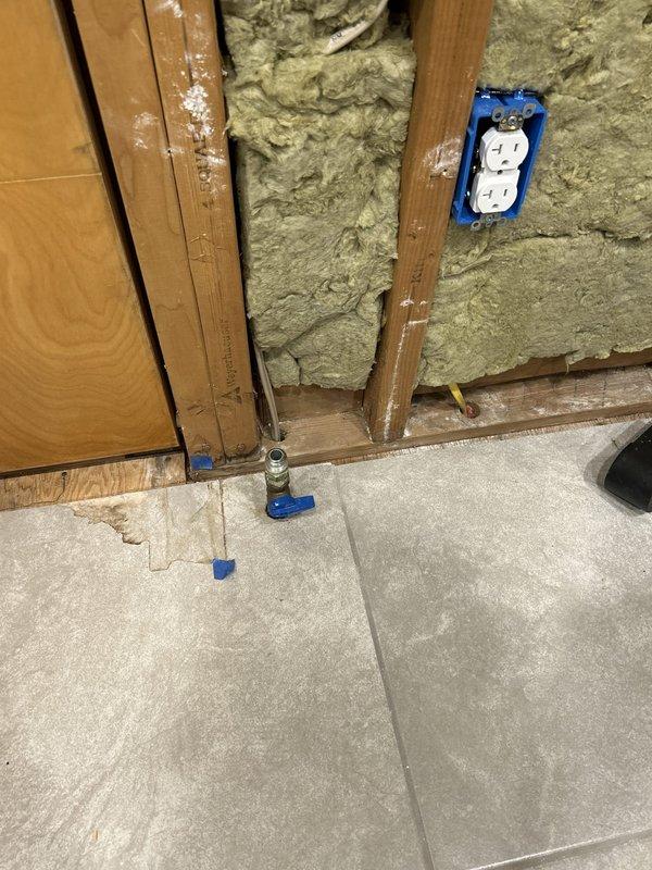 Conducted plumbing inspection to assess feasibility of relocating existing gas line currently penetrating through floor for stove connection. Evaluated gas supply line routing from below floor level through ceiling access point, examining existing pipe configuration, structural framing constraints, and available pathways for potential relocation. Documented current gas line installation with blue-capped supply connections at floor level and traced routing through ceiling cavity where PVC venting, HVAC ductwork, and existing utilities create spatial limitations. Inspection revealed gas line positioning relative to wall framing, insulation, and other mechanical systems to determine modification options and requirements for moving the gas supply connection to desired location.