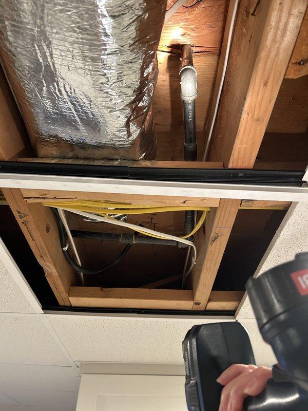 Conducted plumbing inspection to assess feasibility of relocating existing gas line currently penetrating through floor for stove connection. Evaluated gas supply line routing from below floor level through ceiling access point, examining existing pipe configuration, structural framing constraints, and available pathways for potential relocation. Documented current gas line installation with blue-capped supply connections at floor level and traced routing through ceiling cavity where PVC venting, HVAC ductwork, and existing utilities create spatial limitations. Inspection revealed gas line positioning relative to wall framing, insulation, and other mechanical systems to determine modification options and requirements for moving the gas supply connection to desired location.