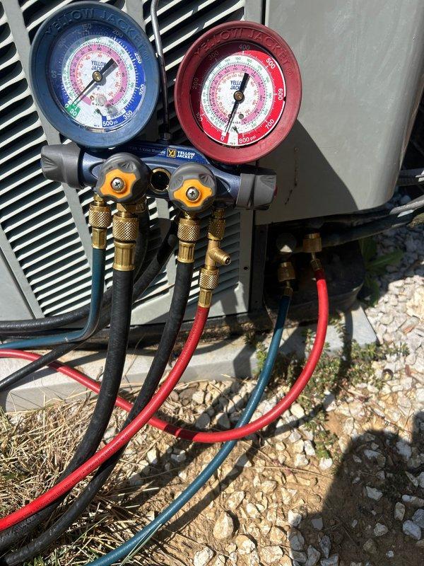 Responded to no cooling complaint on 20-year-old electric air conditioning system with condenser unit not operating. Upon arrival, confirmed indoor unit in basement was running but outdoor condenser remained off. Performed diagnostic testing and connected manifold gauge set to service ports to assess refrigerant pressures and system operation. Identified failed condenser unit preventing proper cooling cycle. Documented system conditions with pressure readings and photographed equipment setup during diagnostic process for service records.
