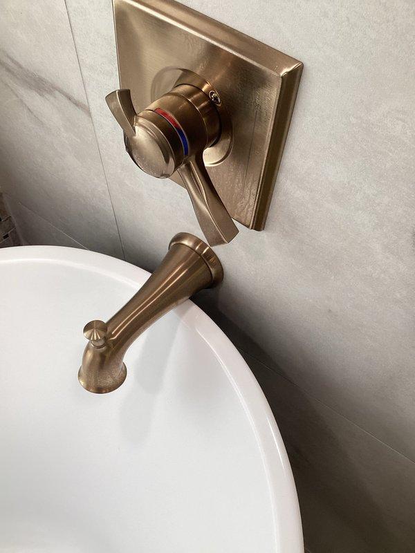 Provided plumbing estimate for replacement of existing tub filler fixture in historic two-story residence built in 1880. Current wall-mounted tub spout and shower valve control feature brushed bronze finish that was installed during previous renovation but does not match other bathroom fixtures. Assessed installation complexity due to fixture mounting behind marble-look tile wall and documented existing configuration including square escutcheon plate with lever handle and wall-mounted spout assembly. Customer expressed concerns regarding proper removal and reinstallation to avoid tile damage during replacement process.